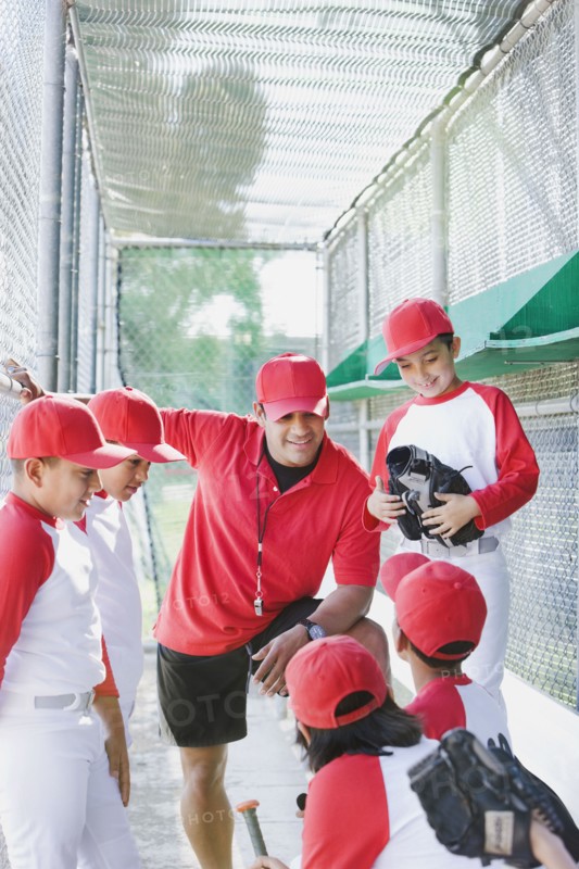Multi-ethnic boys in baseball uniforms with coach in dugout