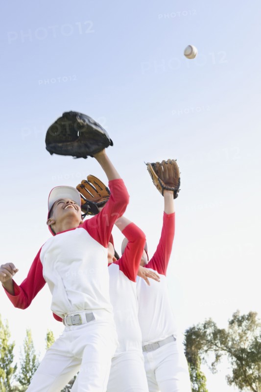 Multi-ethnic boys in baseball uniforms jumping to catch baseball