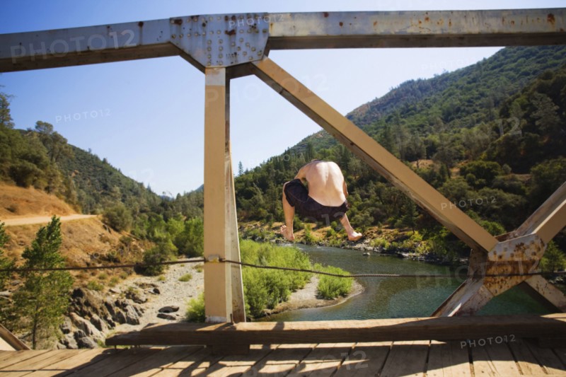 Caucasian man jumping into river from bridge