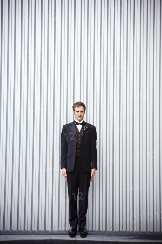 Serious groom standing near wall