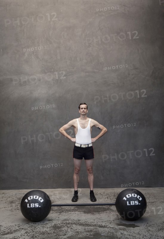 Skinny Caucasian weight lifter standing by weights