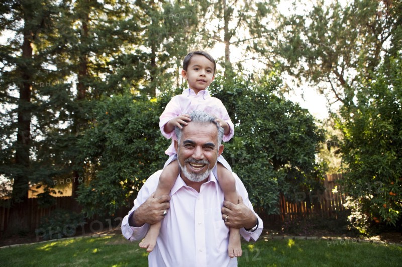 Grandfather carrying grandson on shoulders in backyard