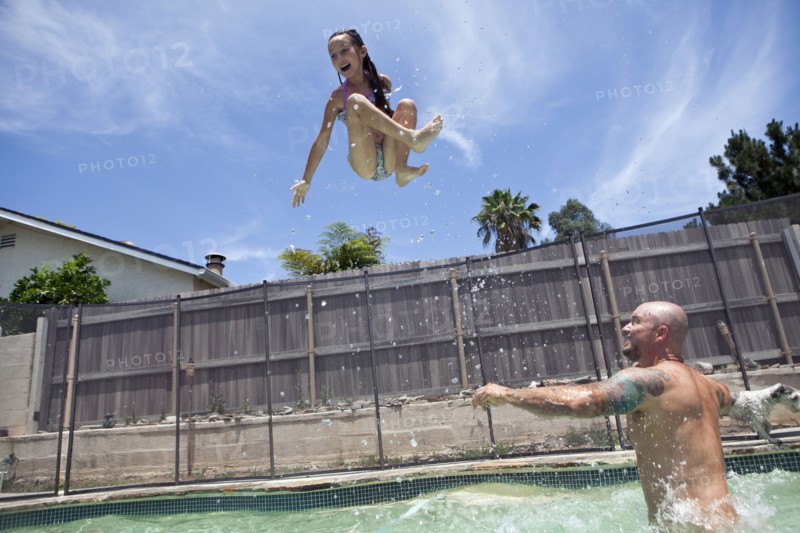 Caucasian father throwing daughter in backyard swimming pool
