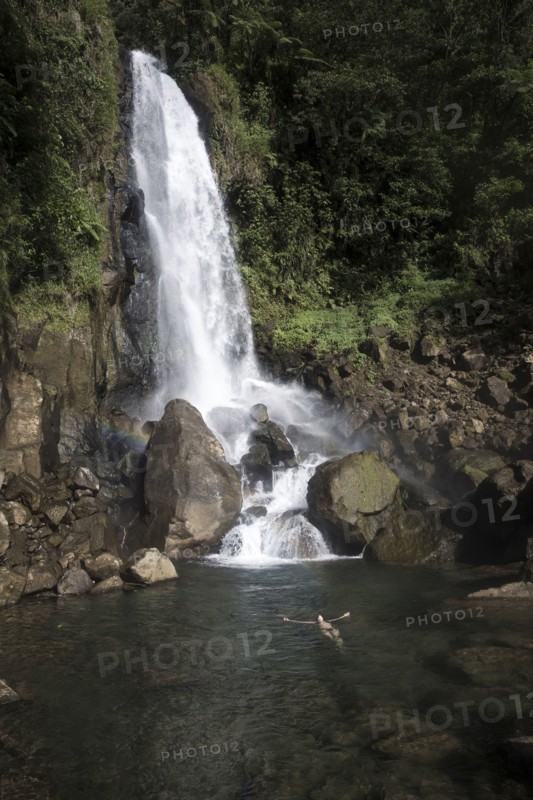 Mixed Race woman swimming in waterfall pool