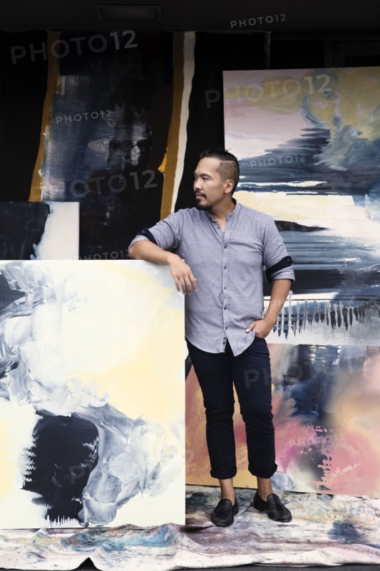 Pacific Islander artist leaning on paintings