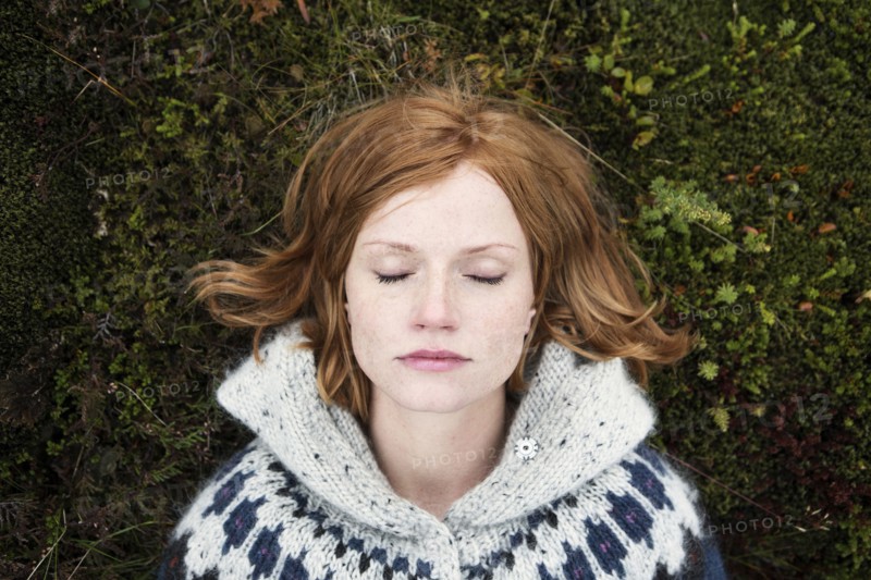 Caucasian woman laying on moss with eyes closed