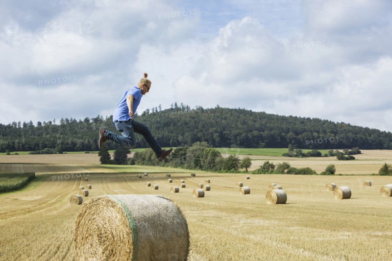 Farmer jumping over hay bale in field