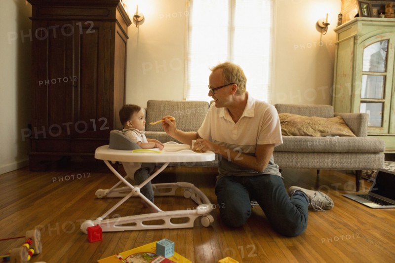Father feeding son in high chair in living room