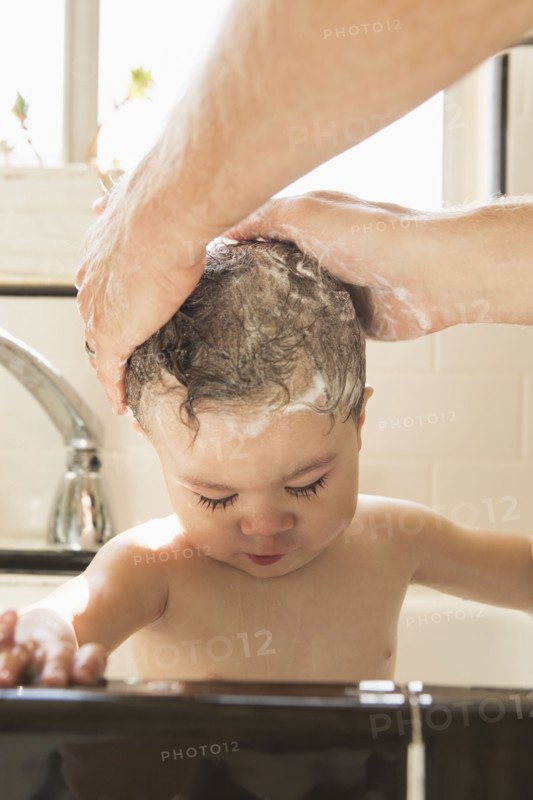 Father washing baby son in kitchen sink
