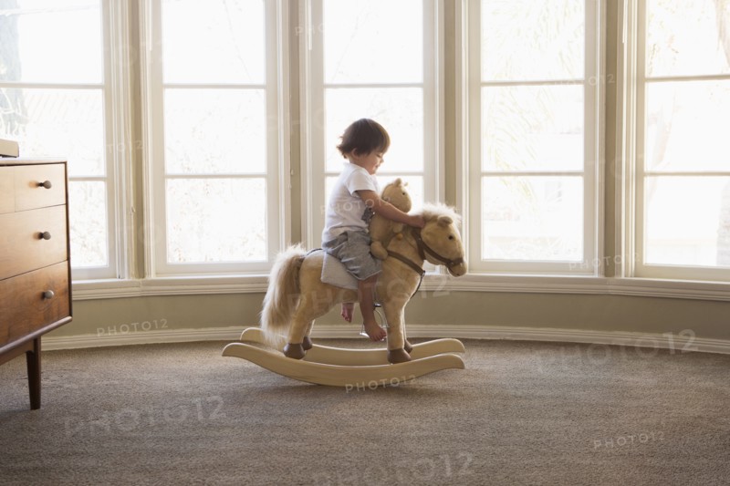Mixed Race boy sitting on rocking horse near window