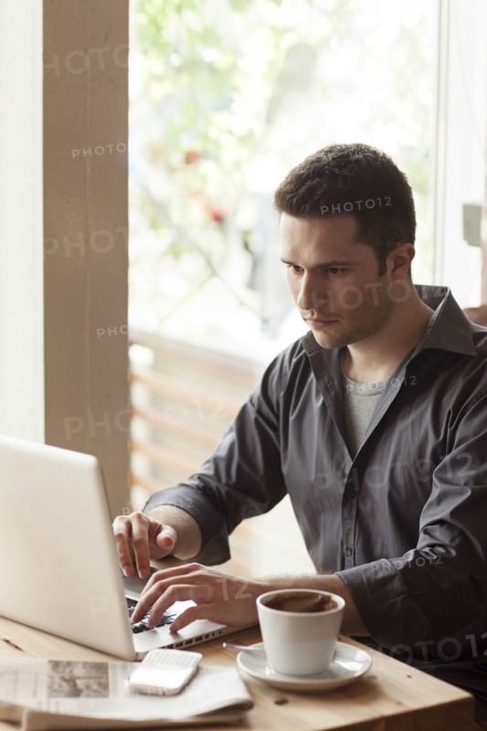 Man using laptop with cup of coffee in cafe