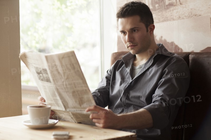 Man reading newspaper and drinking coffee in cafe