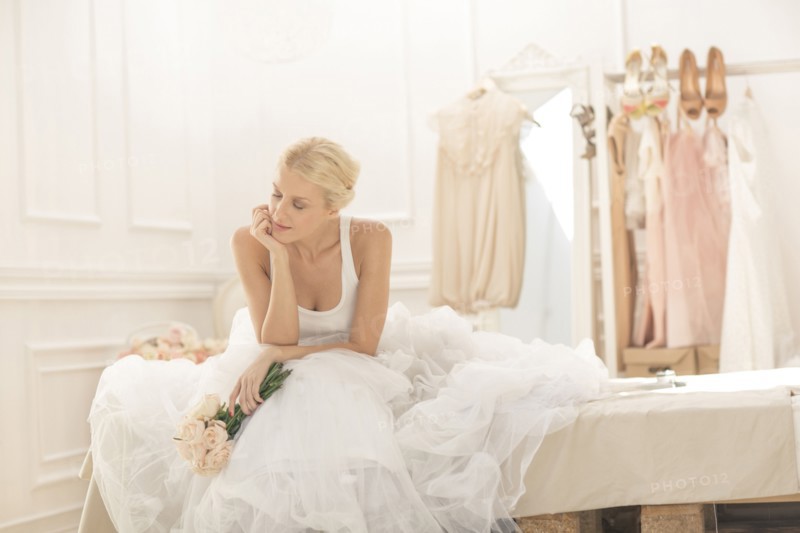 Pensive bride sitting with bouquet on bed