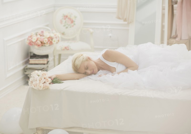 Bride sleeping on bed with bouquet of flowers