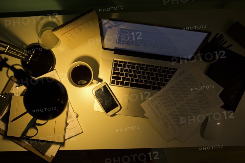 Computer and cell phone illuminated by desk lamp at night