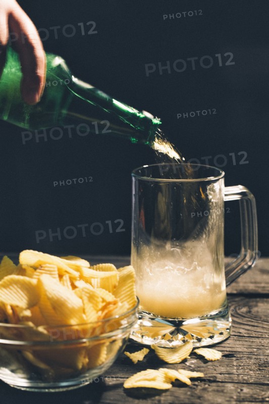 Hand pouring glass of beer near potato chips