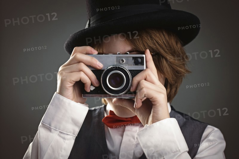 Close up of boy in top hat photographing with vintage camera