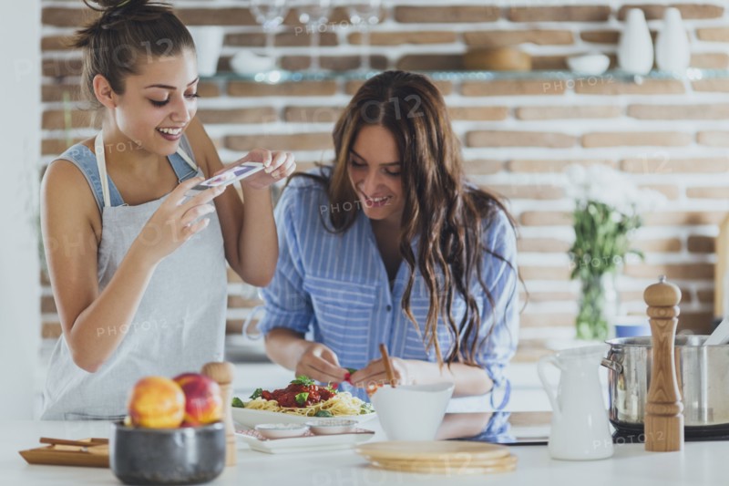 Caucasian women photographing pasta in kitchen