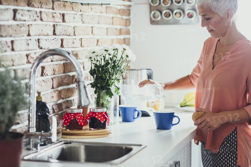 Older Caucasian woman making coffee in kitchen
