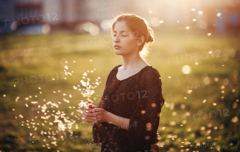 Caucasian woman standing in field with blowing dandelion seeds