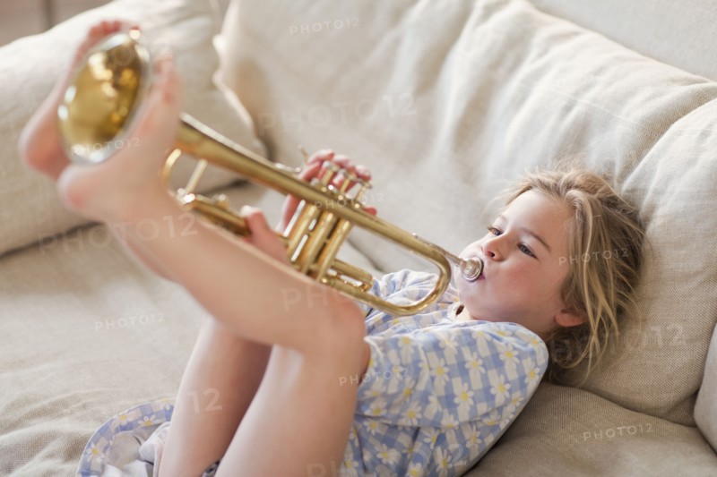 Caucasian girl on sofa playing trumpet