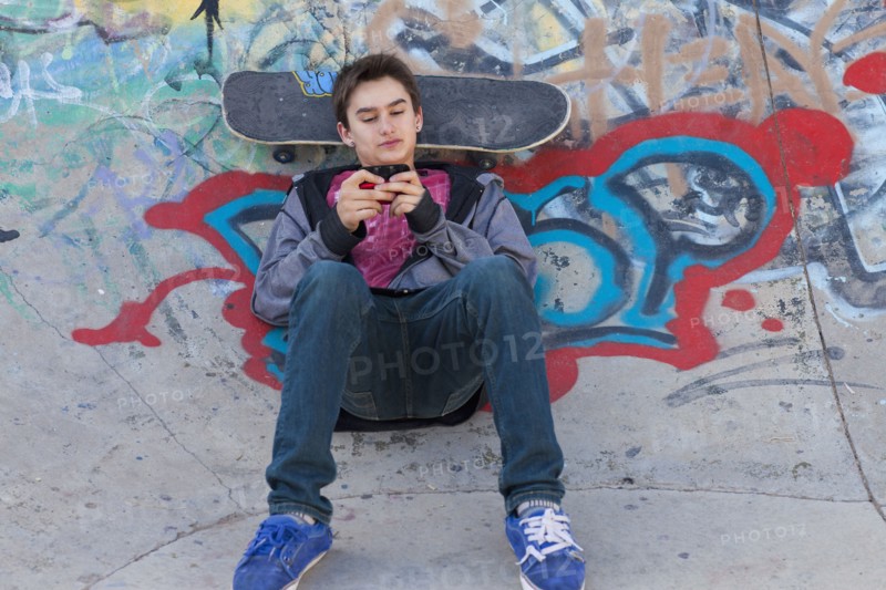 Mixed race boy with skateboard text messaging on cell phone