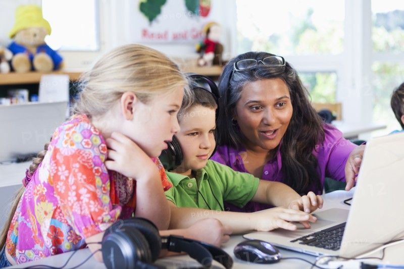 Teacher helping students using laptop