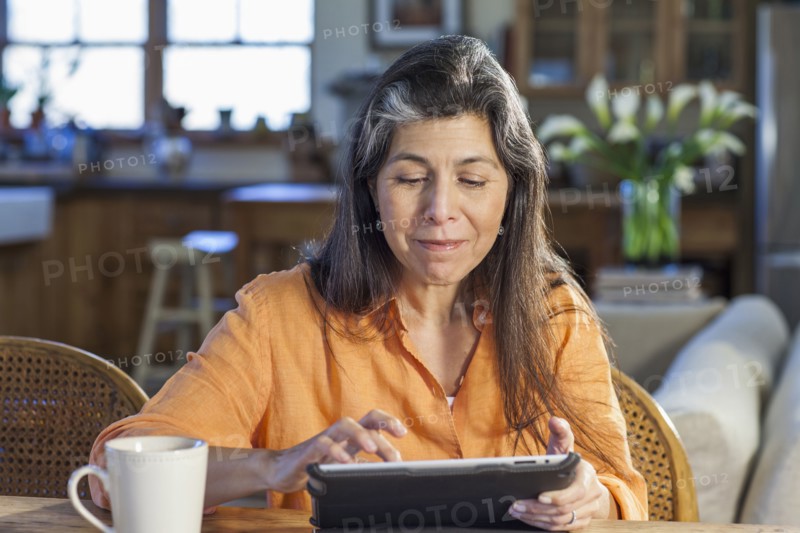 Older Hispanic woman using tablet computer at table