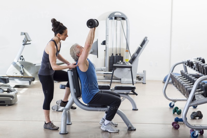 Older Hispanic man working with trainer in gym