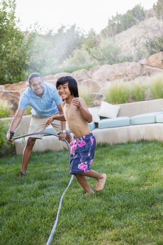 Father and son playing with hose in backyard