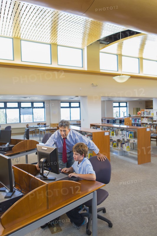 Teacher and student working at computer in library