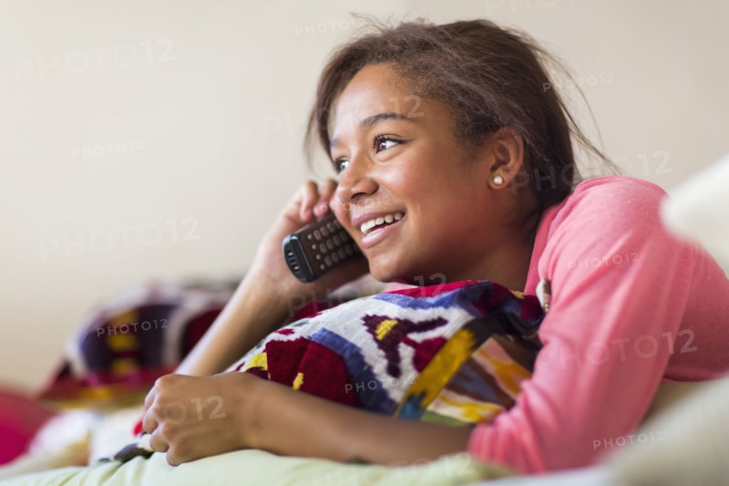 Mixed race teenage girl talking on telephone on bed