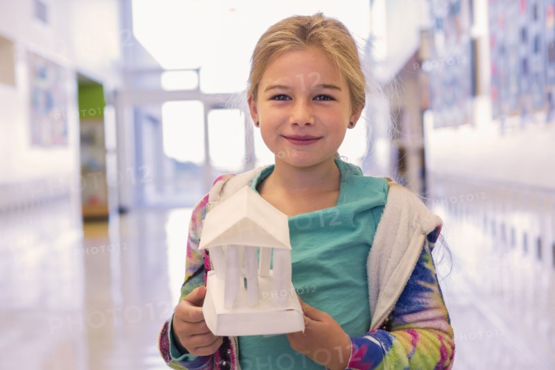 Caucasian girl holding art project in school corridor