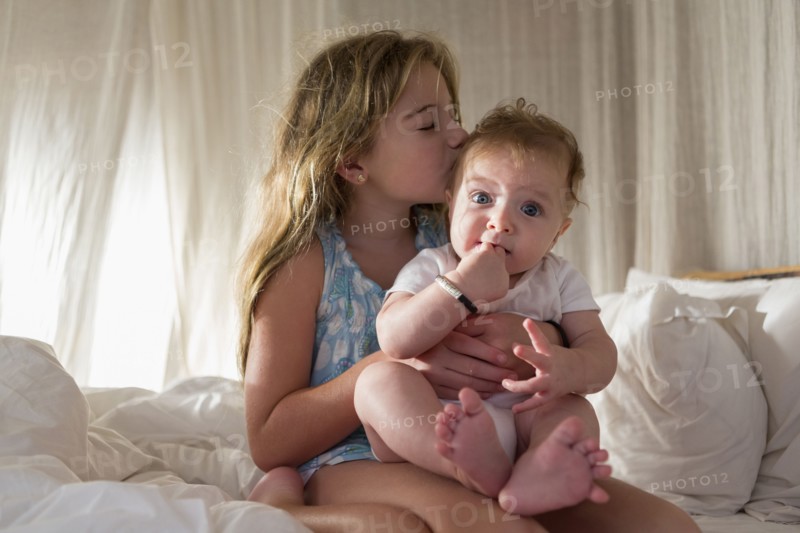 Caucasian girl kissing sibling on sofa