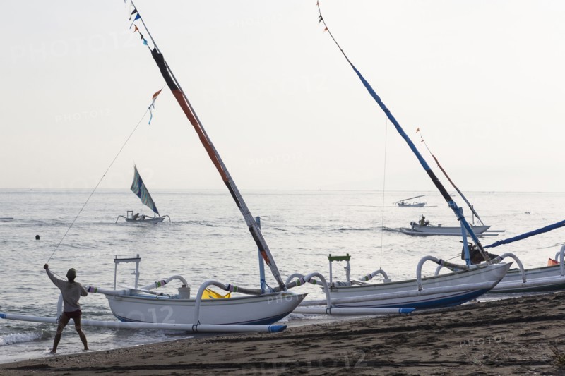 Fisherman pulling sailboat line on beach