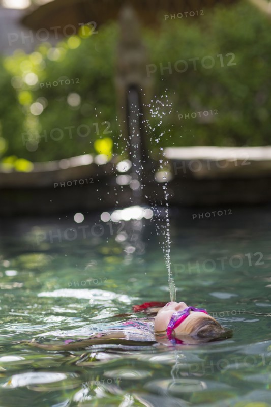 Caucasian girl spraying water in swimming pool
