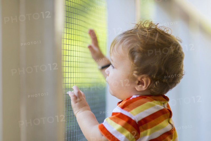 Caucasian toddler peering out screen door