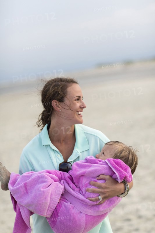 Caucasian mother carrying daughter on beach