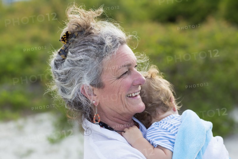 Caucasian woman carrying grandson on beach