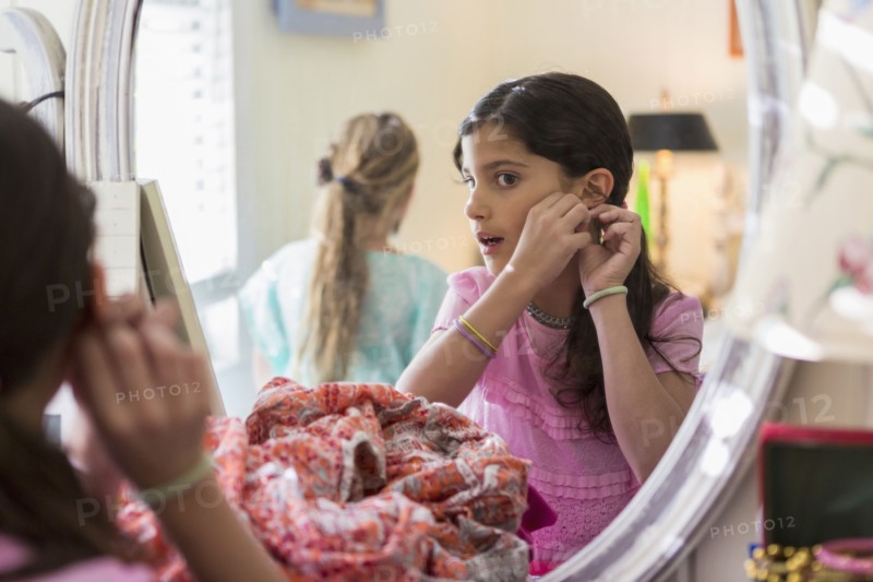 Girls putting on earrings in bedroom