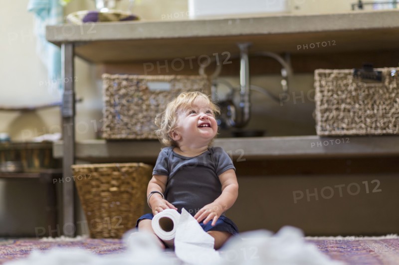 Caucasian baby unraveling toilet paper in bathroom