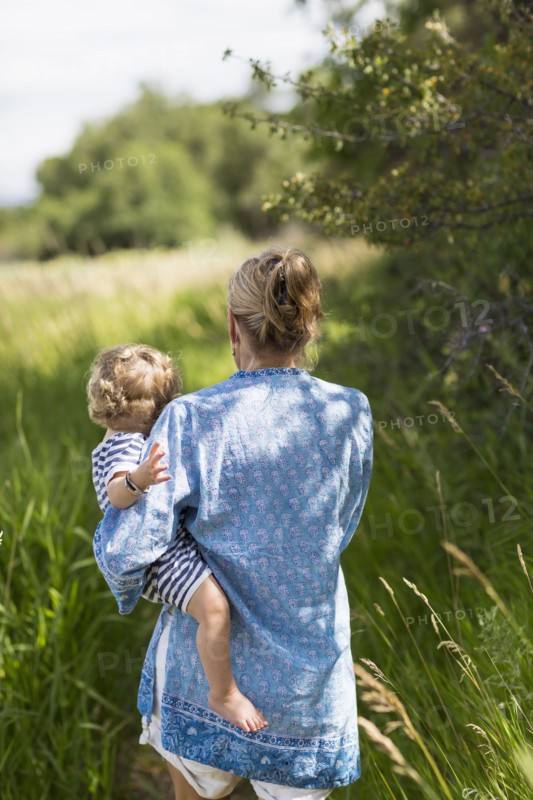 Caucasian mother carrying baby son in grassy field