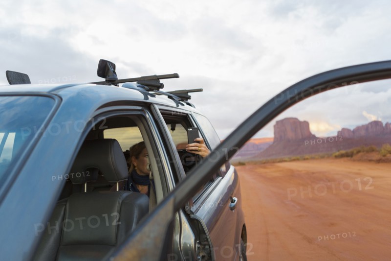 Caucasian girl taking cell phone photograph from car