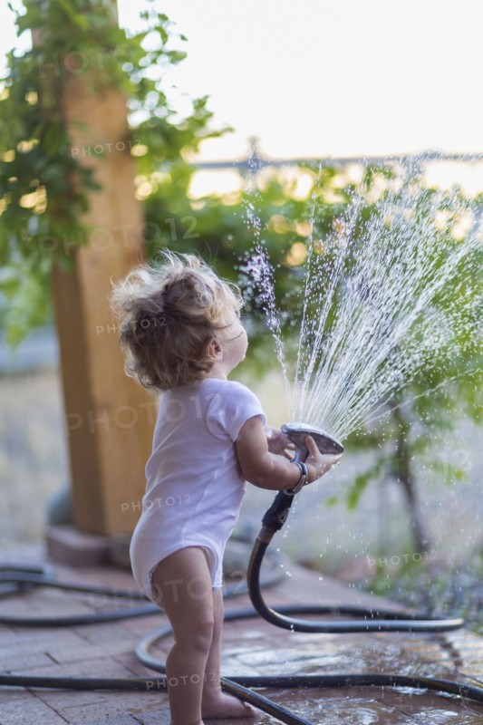 Caucasian baby boy playing with hose on patio