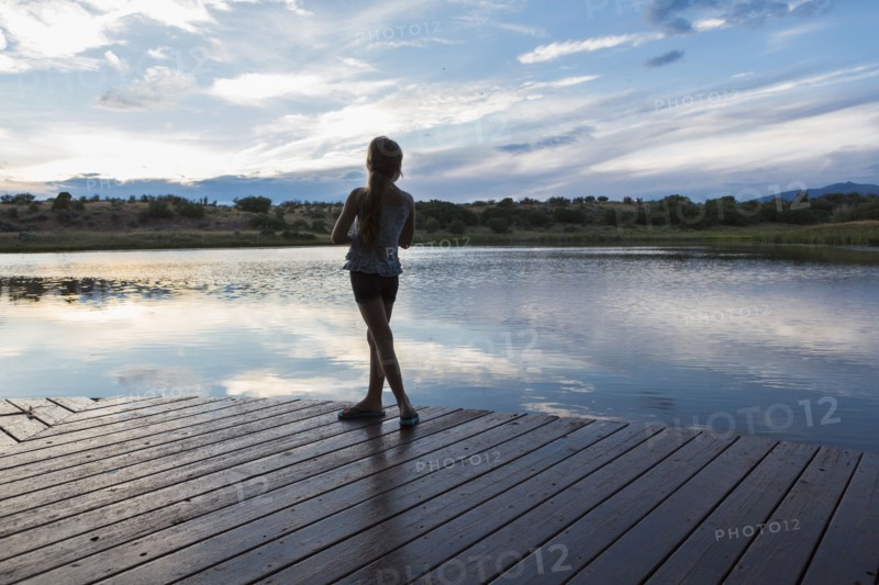 Caucasian girl standing on wooden deck near lake