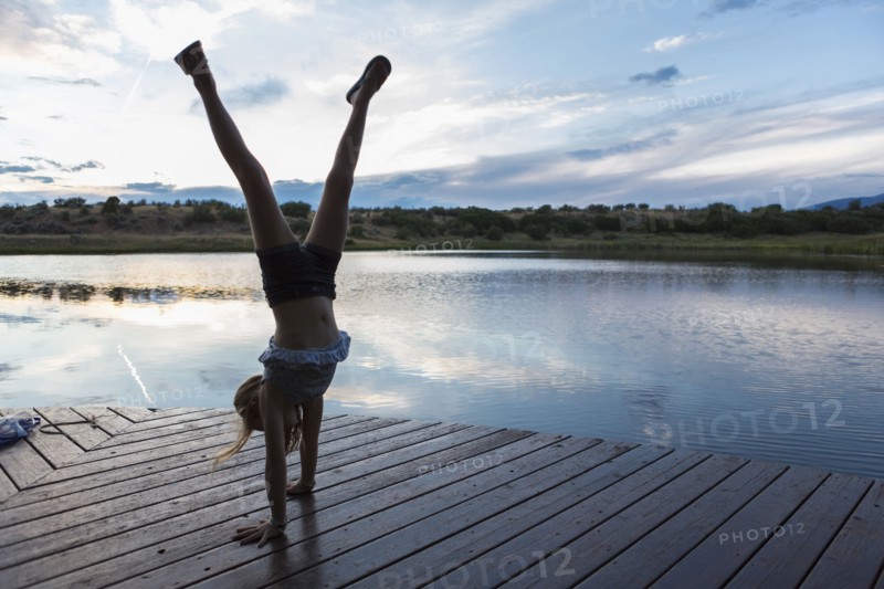 Caucasian girl doing handstand on wooden deck near lake