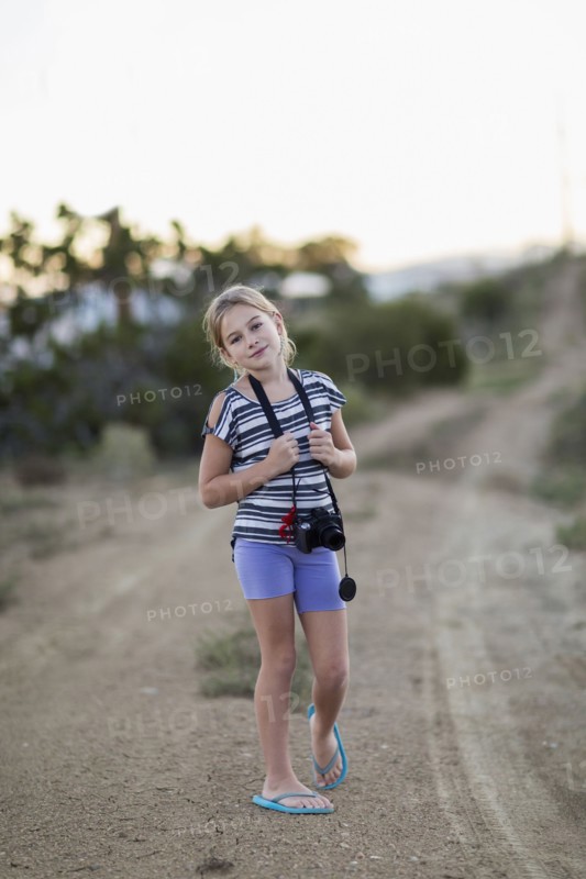 Caucasian girl carrying camera on rural dirt road
