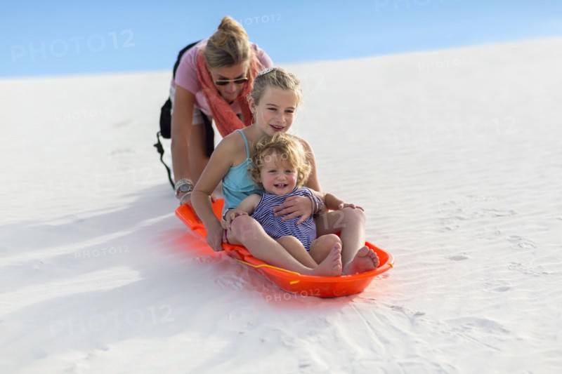 Caucasian mother and children sledding on sand dune