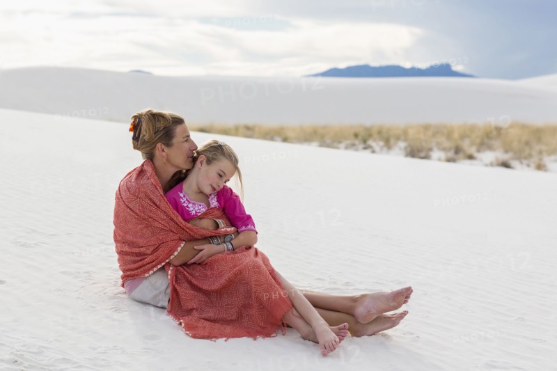 Caucasian mother and daughter wrapped in blanket on sand dune