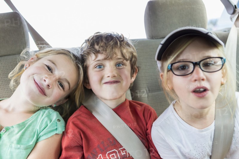 Caucasian children smiling in back seat of car